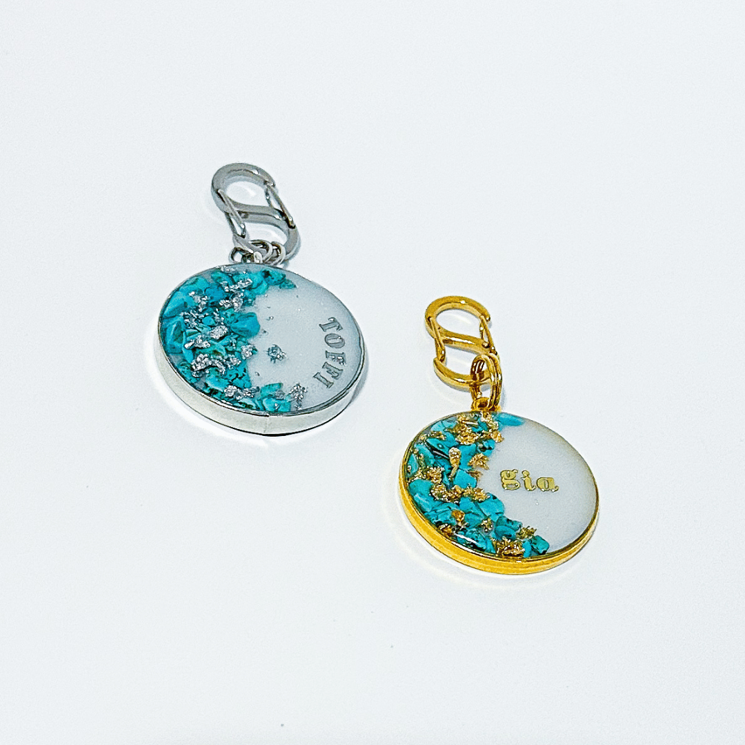 Shimmery white round pet ID tag with silver stainless steel hardware, turquoise blue stones and silver foil, shimmery white round pet ID tag with gold-plated stainless steel hardware, turquoise blue stones and gold flake.