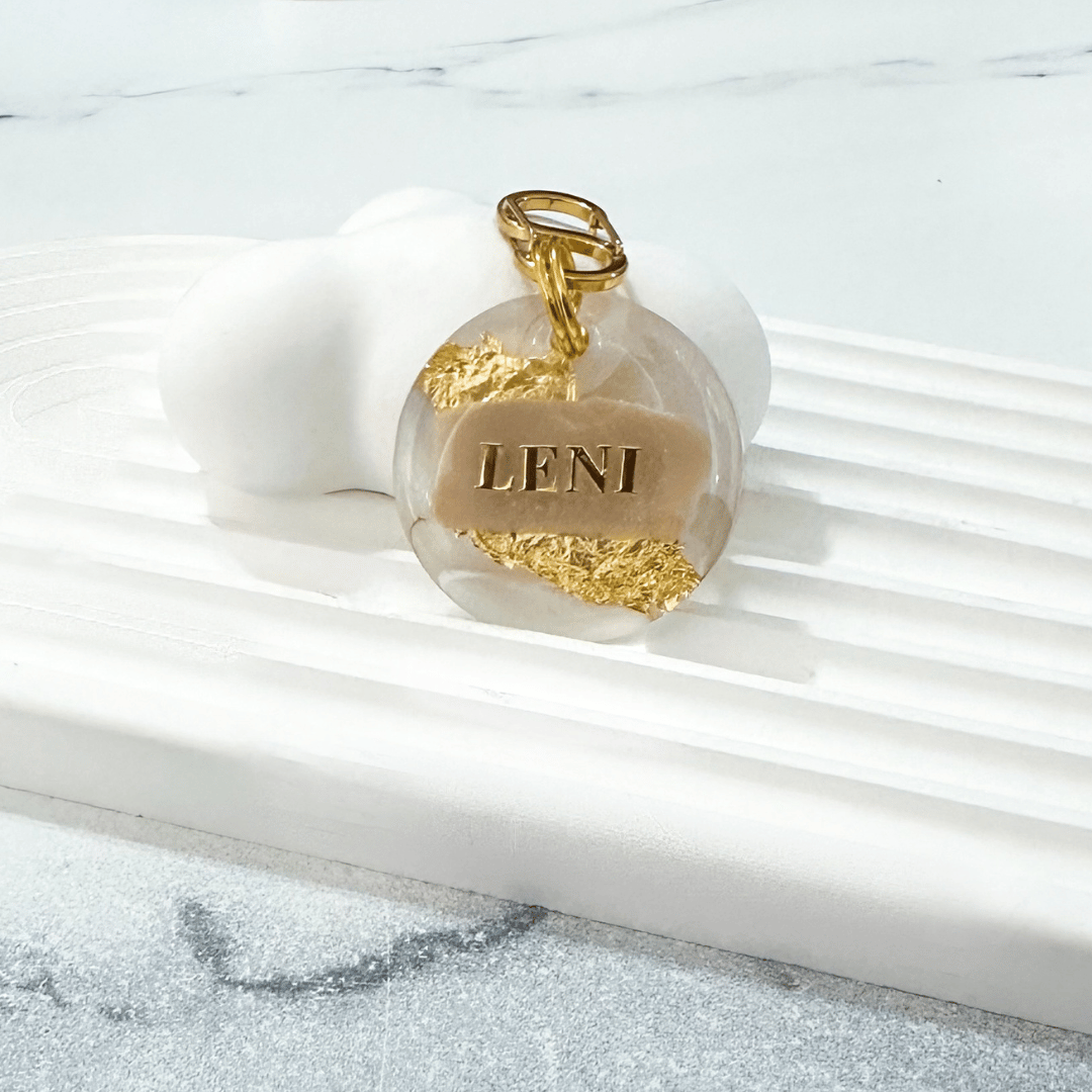 Round pet ID tag with clear resin, beige, gold leaf, and gold-plated stainless steel hardware, complimentary gold-plated stainless steel S-clasp.