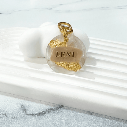 Round pet ID tag with clear resin, beige, gold leaf, and gold-plated stainless steel hardware, complimentary gold-plated stainless steel S-clasp.