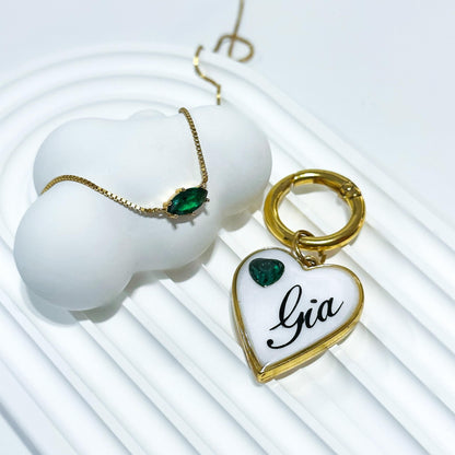 White heart-shaped pet ID tag with gold-plated stainless steel hardware and emerald green heart-shaped cubic zirconia crystal.